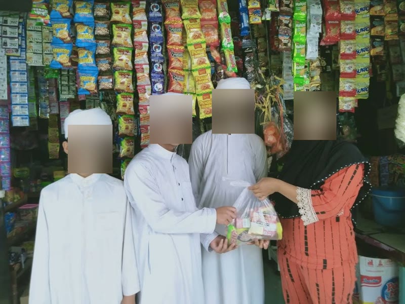 Tiga santri bersorban putih bersama pemilik warung di depan rak jajanan, memegang bingkisan bersama