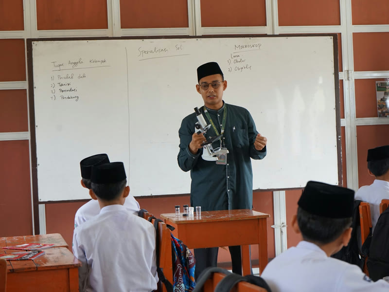 Ustadz menjelaskan bagian mikroskop di depan papan tulis kepada santri yang duduk di kelas