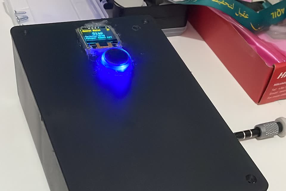 Kotak absensi hitam dengan layar OLED dan sensor sidik jari yang menyala biru