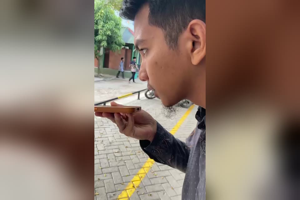 Petugas mendikte pengumuman ke HP di halaman pondok, santri berjalan di latar belakang